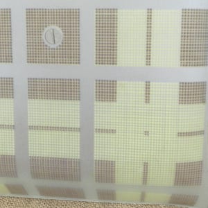 May include: A translucent, rectangular object with a grid pattern. The grid features alternating squares of light yellow and brown, overlaid with a series of white lines. A small, circular fastener is visible near the top.