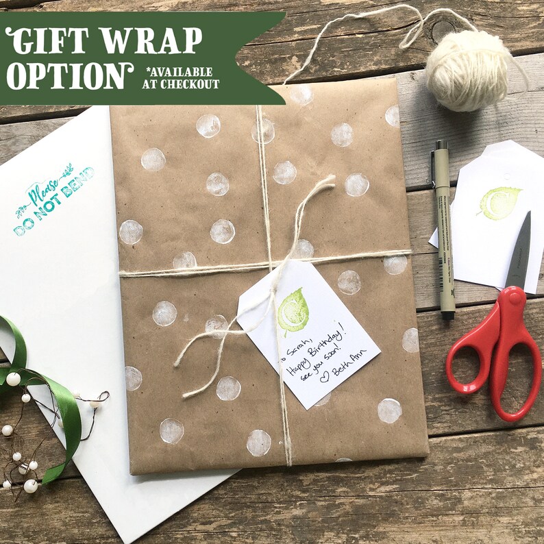 K&ouml;nnte beinhalten: Ein Geschenk in braunem Papier mit wei&szlig;en Punkten, mit Bindfaden verschn&uuml;rt. Ein Geschenkanh&auml;nger mit einem gr&uuml;nen Blattmuster und handschriftlicher Nachricht ist angebracht. Die Worte "GIFT WRAP OPTION" stehen oben. Ein wei&szlig;er Umschlag und eine Schere sind ebenfalls sichtbar.