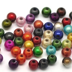 Könnte beinhalten: Eine Sammlung bunter runder Perlen mit einem metallischen Schimmer. Die Perlen sind in verschiedenen Schattierungen von Grün, Blau, Rot, Gold und Lila.