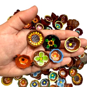 May include: A hand holding a collection of small, colorful, hand-painted ceramic bowls. The bowls are decorated with floral designs and feature various colors, including red, blue, yellow, green, and brown.