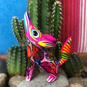 K&ouml;nnte beinhalten: Eine farbenfrohe Holzfigur eines Kojoten mit rosa, gelber, blauer, roter und gr&uuml;ner Farbe. Der Kojote steht auf seinen Hinterbeinen, den Kopf nach oben geneigt und den Mund offen.