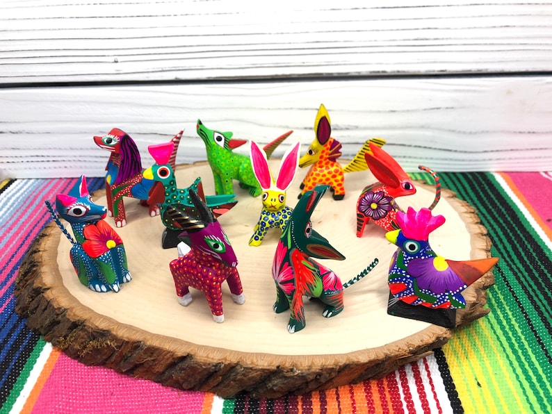 May include: A collection of ten hand-painted wooden animal figurines. The figurines are brightly colored and feature a variety of animals, including a rooster, a rabbit, a cat, and a dog. The figurines are arranged on a wooden slice.