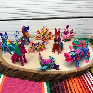 May include: A collection of colorful, hand-painted wooden animal figurines. The figurines include a cat, dog, pig, fish, rooster, peacock, and two other animals. The figurines are arranged on a wooden slice.
