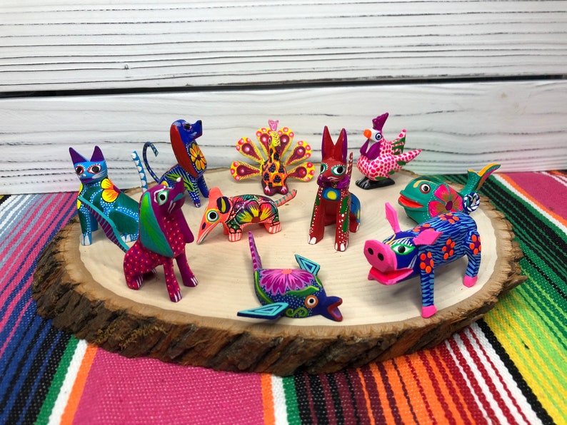 May include: A collection of colorful, hand-painted wooden animal figurines. The figurines include a cat, dog, pig, fish, rooster, peacock, and two other animals. The figurines are arranged on a wooden slice.