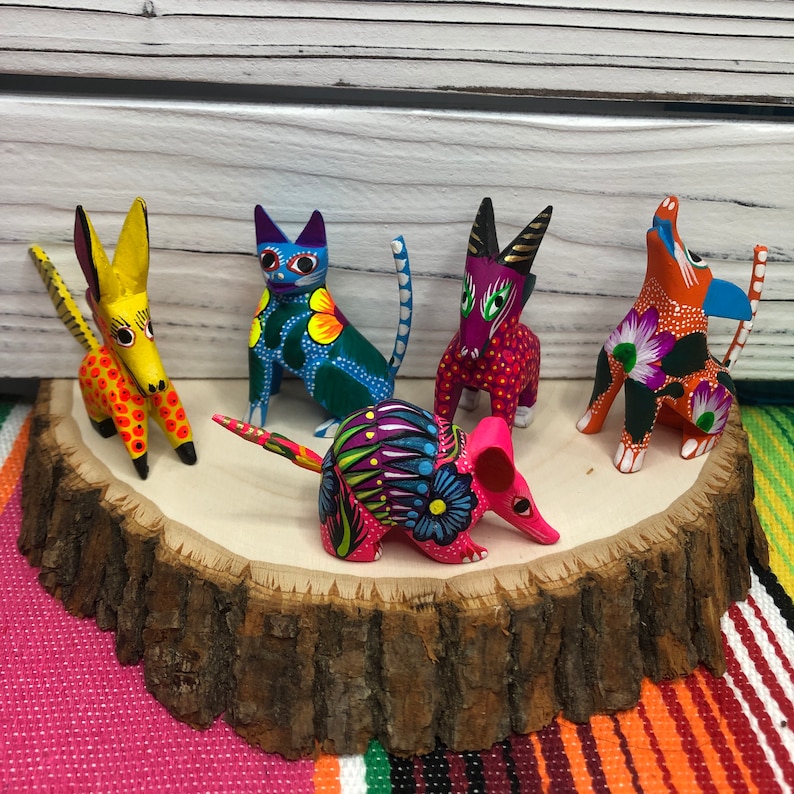K&ouml;nnte beinhalten: F&uuml;nf bunte, handbemalte Holztierfiguren, darunter eine Katze, ein Hund, ein Esel, ein G&uuml;rteltier und ein Vogel, werden auf einer Holzscheibe pr&auml;sentiert. Die Figuren sind leuchtend bunt und mit aufwendigen Details verziert.