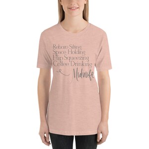 May include: A light pink t-shirt with the text "Rebozo Sifting Space Holding Hip Squeezing Coffee Drinking Midwife" printed in grey.