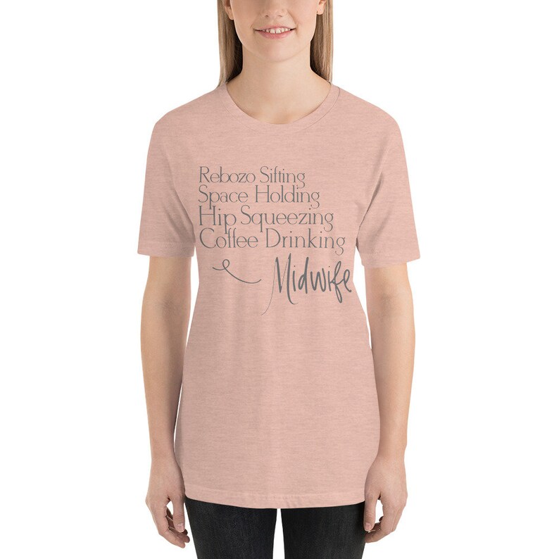 May include: A light pink t-shirt with the text "Rebozo Sifting Space Holding Hip Squeezing Coffee Drinking Midwife" printed in grey.