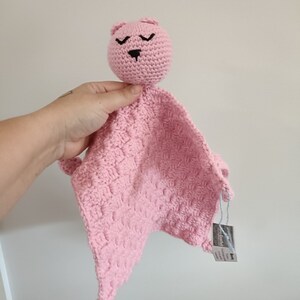 Könnte beinhalten: Rosa gehäkelte Babydecke mit einem rosa gehäkelten Bärenkopf. Der Bär hat schwarze Augen und eine schwarze Nase.
