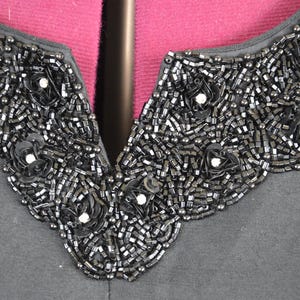 May include: A black shirt with a beaded neckline. The beads are arranged in a floral pattern.
