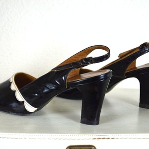 May include: A pair of black heeled shoes with white scalloped trim around the toe. The shoes have a slingback strap with a buckle closure.