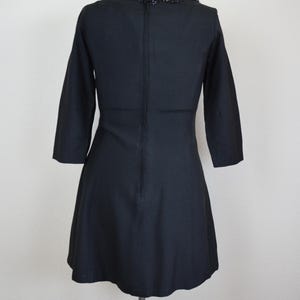 May include: A black dress with a beaded neckline. The dress has a fitted bodice and a flared skirt. The dress is on a mannequin.