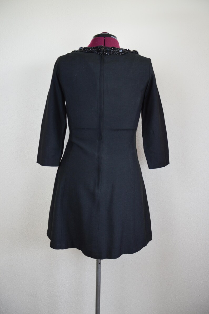 May include: A black dress with a beaded neckline. The dress has a fitted bodice and a flared skirt. The dress is on a mannequin.