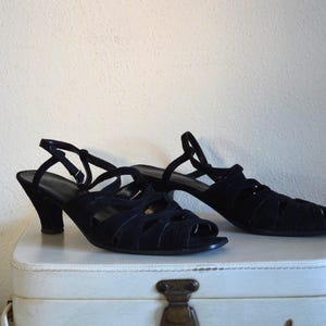 May include: A pair of black open-toe sandals with a heel. The sandals have multiple straps across the top and a strap that goes around the ankle. The heels are approximately 2.5 inches high.