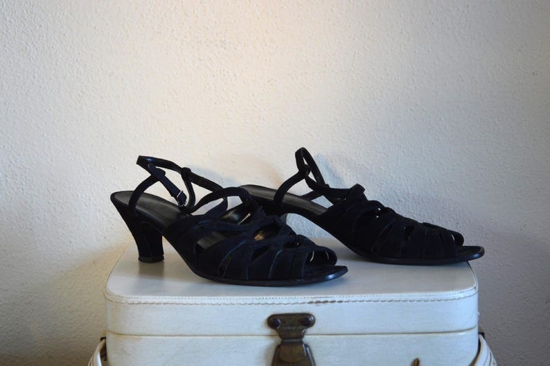 May include: A pair of black open-toe sandals with a heel. The sandals have multiple straps across the top and a strap that goes around the ankle. The heels are approximately 2.5 inches high.