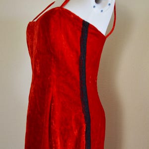 May include: A red velvet dress with spaghetti straps and a dark blue lace trim down the side. The dress is displayed on a white mannequin. The fabric has a textured appearance.