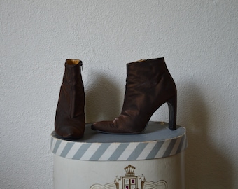 May include: Two pairs of brown satin ankle boots with high heels. The boots are on a striped box.
