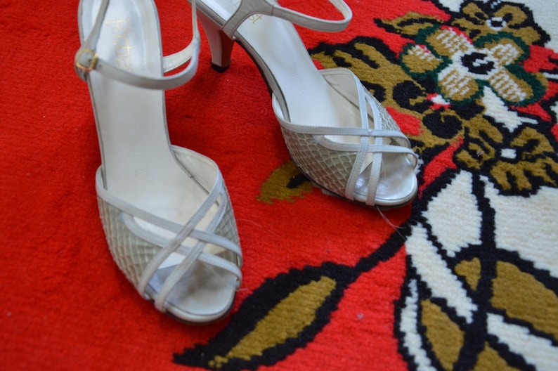 Puede incluir: Un par de sandalias de tac&oacute;n color blanco roto con un dise&ntilde;o de tiras cruzadas sobre la puntera abierta y una tira fina en el tobillo con una hebilla dorada. La parte delantera del zapato est&aacute; hecha de un material de malla tejida texturizada.