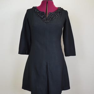 May include: A black dress with a beaded neckline and three-quarter sleeves. The dress has a fitted bodice and a slightly flared skirt.
