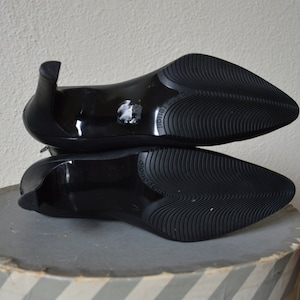 May include: A pair of black heeled shoes with a pointed toe and a textured rubber sole. The shoes are stacked on top of each other.