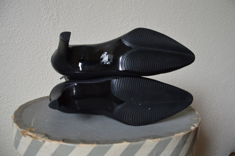 May include: A pair of black heeled shoes with a pointed toe and a textured rubber sole. The shoes are stacked on top of each other.