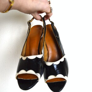 May include: A pair of black and white heeled shoes with a scalloped edge. The shoes are open-toed and have a slingback strap.