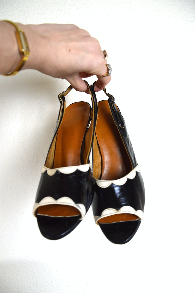 May include: A pair of black and white heeled shoes with a scalloped edge. The shoes are open-toed and have a slingback strap.