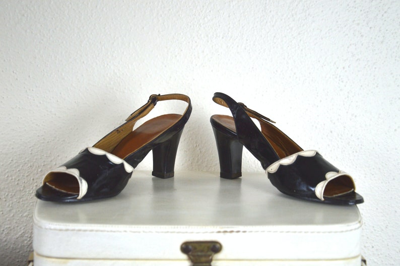 May include: A pair of black and white heeled shoes with a scalloped edge. The shoes have a slingback strap and a closed toe.