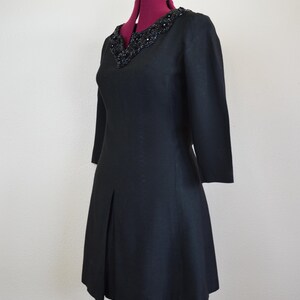 May include: A black dress with a beaded neckline and a-line skirt. The dress has three-quarter sleeves and is made of a textured fabric.