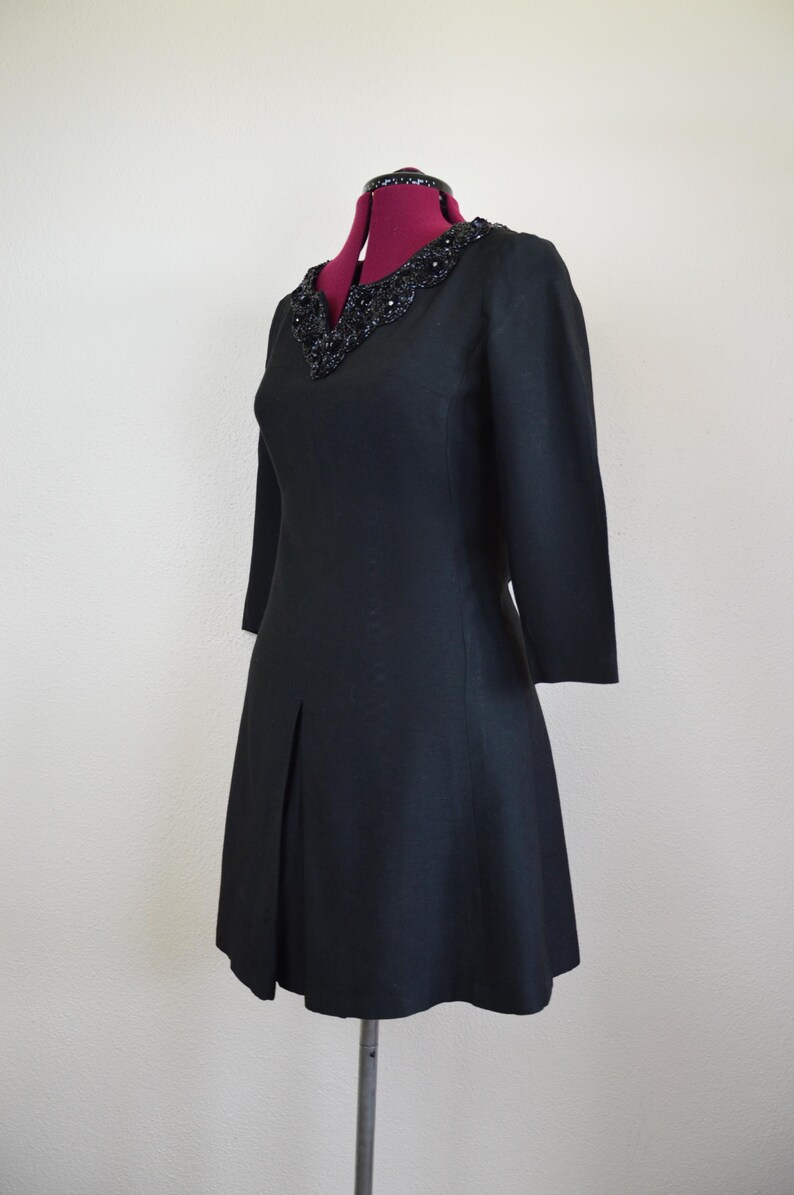 May include: A black dress with a beaded neckline and a-line skirt. The dress has three-quarter sleeves and is made of a textured fabric.