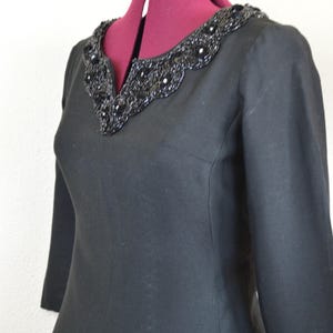 May include: A black dress with a beaded neckline. The dress has three-quarter sleeves and a fitted silhouette.