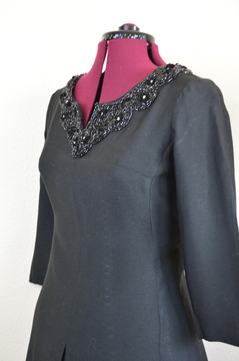 May include: A black dress with a beaded neckline. The dress has three-quarter sleeves and a fitted silhouette.