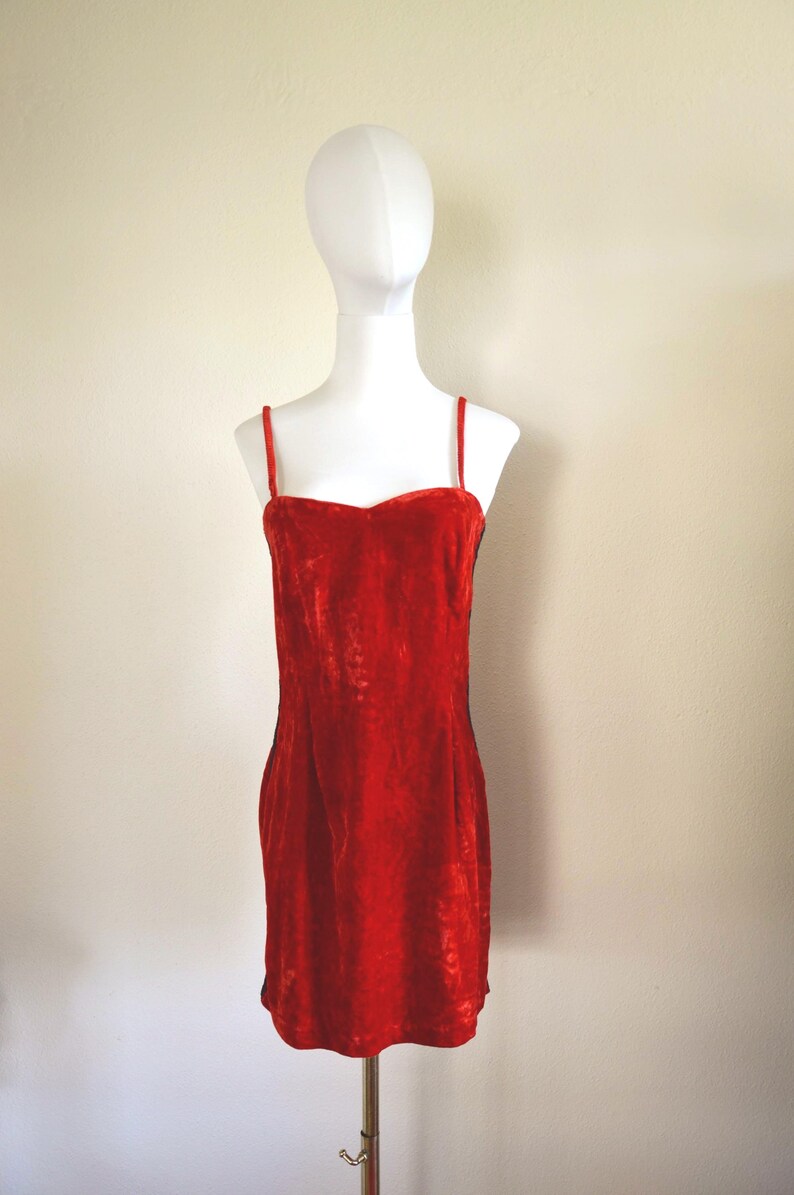 May include: A vibrant red velvet dress with thin straps and a sweetheart neckline. The dress is displayed on a white mannequin, showcasing its form-fitting silhouette. The dress is approximately 86 cm long.
