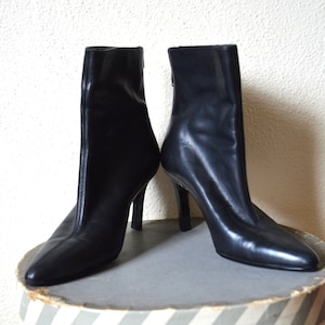 May include: A pair of black leather ankle boots with stiletto heels. The boots have a pointed toe and a zipper on the back.