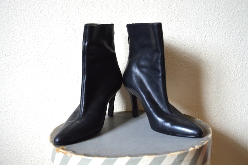 May include: A pair of black leather ankle boots with stiletto heels. The boots have a pointed toe and a zipper on the back.