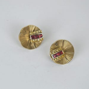 Könnte beinhalten: Ein Paar goldfarbene Ohrringe mit einem roten und klaren Strassstein-Design. Die Ohrringe sind fächerförmig.