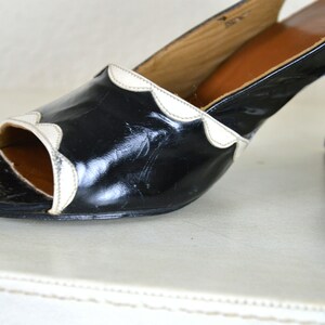 May include: Black leather heeled shoes with a white scalloped trim around the opening. The shoes have a closed toe and a peep toe design.