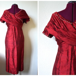 Puede incluir: Un vestido rojo sin mangas con un corpiño drapeado y ribete de cuentas. El vestido está hecho de una tela sedosa y tiene una silueta ajustada.