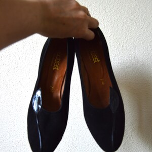 May include: A pair of black suede shoes with a leaf design on the toe. The shoes are labeled "attiest" and have a size of 7 1/2.