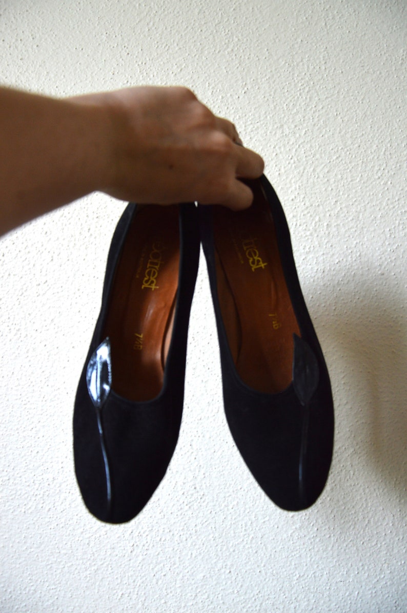 May include: A pair of black suede shoes with a leaf design on the toe. The shoes are labeled "attiest" and have a size of 7 1/2.