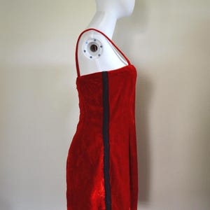 May include: A red velvet mini-dress with thin straps and a dark blue vertical stripe. The dress is displayed on a mannequin. The dress is a classic, simple design.
