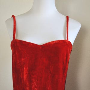 May include: A red velvet dress with thin spaghetti straps. The dress has a sweetheart neckline and is displayed on a white mannequin. The fabric appears soft and luxurious, with a slight sheen.