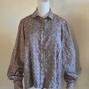 May include: A button-down shirt with a repeating black and white floral pattern. The long-sleeved shirt has a collared neckline and buttoned cuffs. The shirt is displayed on a mannequin.
