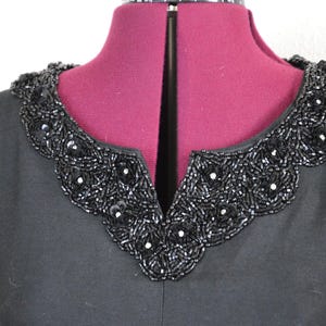 May include: A black dress with a beaded collar. The collar is made of black beads and has a scalloped edge.