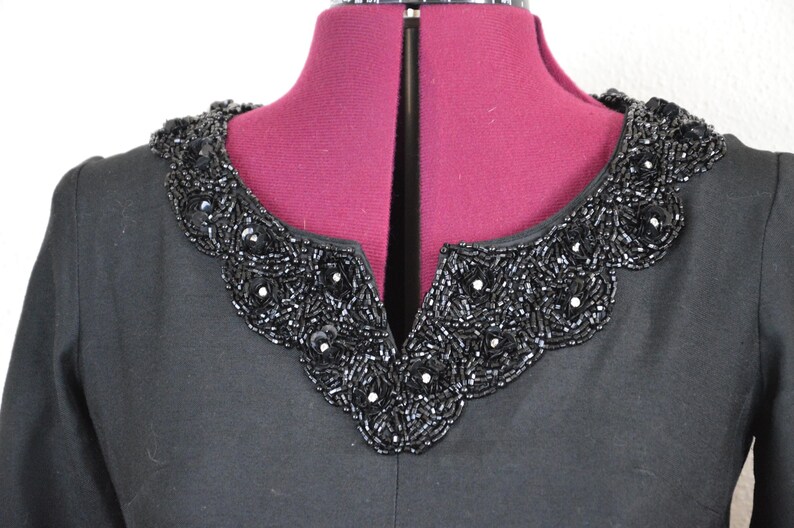 May include: A black dress with a beaded collar. The collar is made of black beads and has a scalloped edge.