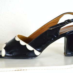 May include: Black and white slingback heels with a scalloped edge detail. The heels are made of patent leather and have a high block heel.