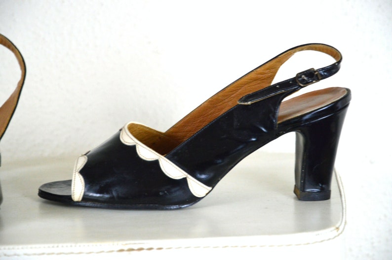 May include: Black and white slingback heels with a scalloped edge detail. The heels are made of patent leather and have a high block heel.