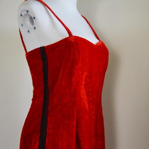 May include: A striking red velvet dress featuring delicate spaghetti straps and a sweetheart neckline. A black stripe adorns the side. The dress is presented on a white mannequin.
