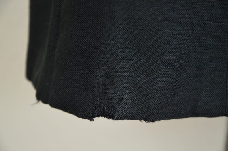 May include: Close-up of the bottom edge of a black blazer. The fabric has a slight texture and there is a small tear in the fabric.