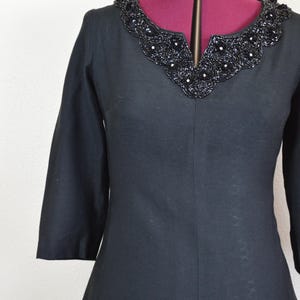 May include: A black dress with a beaded neckline. The dress has a v-neck and three-quarter sleeves.