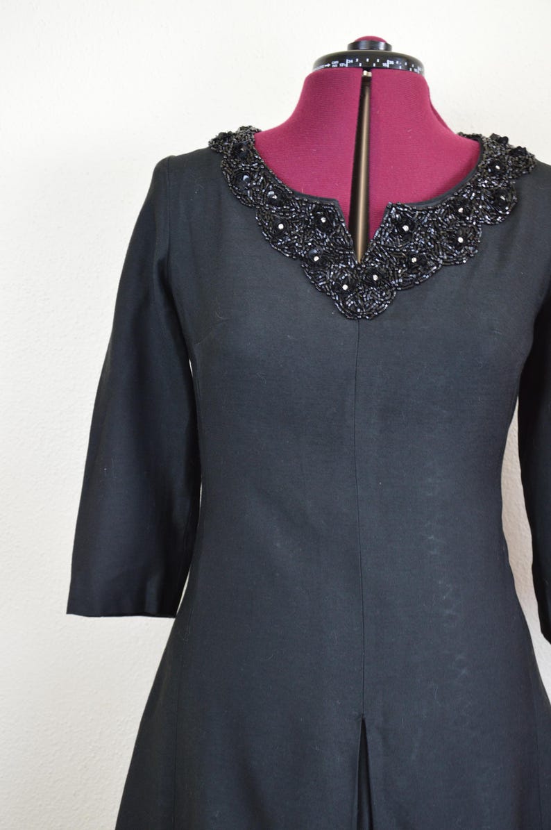 May include: A black dress with a beaded neckline. The dress has a v-neck and three-quarter sleeves.